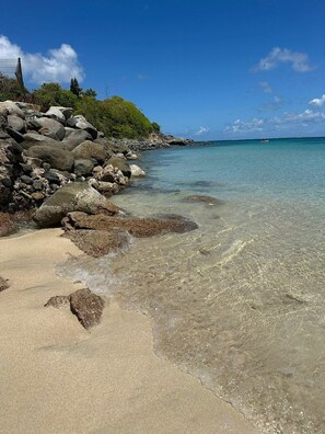 A beach with clear water, rocks, and a distant boat. - Beautiful loft in the heart of Marigot with a view of Anguilla (Marigot)