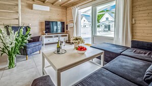 Una sala moderna con un conjunto de sofá, una mesa de centro, un televisor y una ventana con vista a una casa.