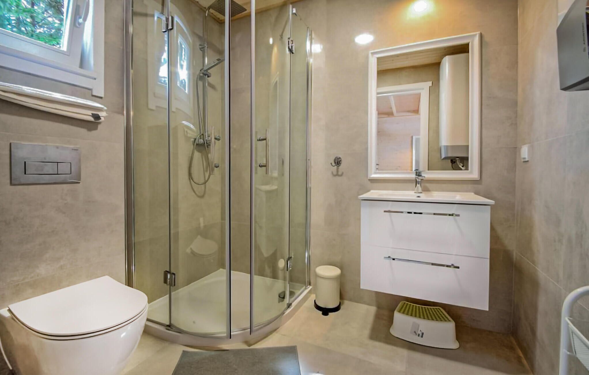 A modern bathroom with a glass-enclosed shower, a white toilet, a vanity with a mirror, and a small trash bin.