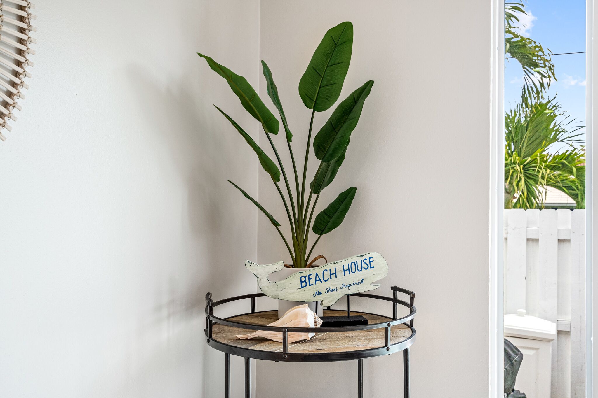 A potted plant with a sign reading "Beach House No Shoes Required" on a metal stand.