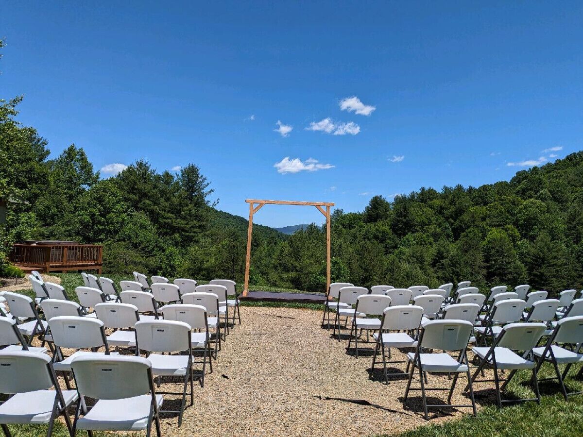 An outdoor wedding venue with rows of white chairs and a wooden archway.