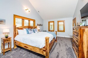 Un dormitorio con una cama de madera, dos mesitas de noche, un aparador y un televisor.