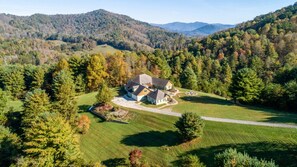A large house surrounded by a well-maintained lawn and trees, with a hilly landscape in the background.