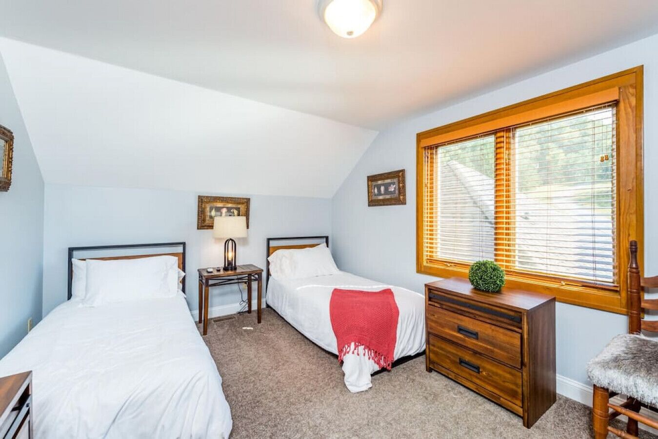 A bedroom with two single beds, a nightstand with a lamp, a dresser, and a window with blinds.