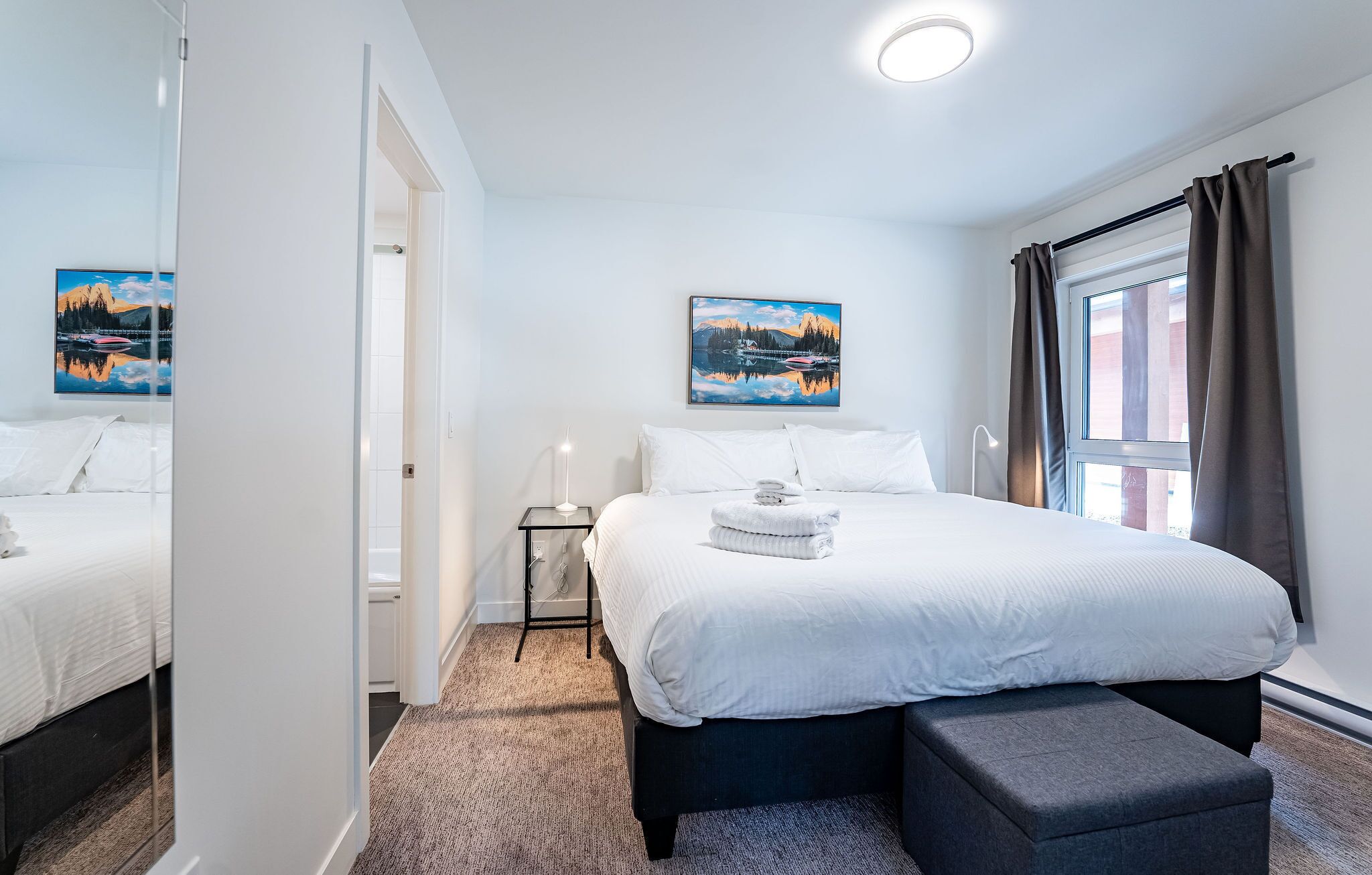 Ein Hotelzimmer mit einem großen Bett, einem Nachttisch, einem Fenster mit Vorhängen und zwei Bildern an der Wand.