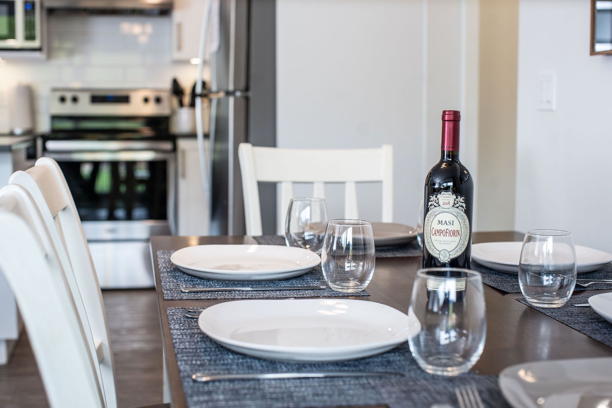 Une table à manger dressée avec des assiettes, des verres et une bouteille de vin, dans une cuisine moderne.