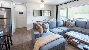 Una sala de estar moderna con un sofá seccional gris, una mesa de centro de madera y un comedor con mesa y sillas.