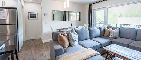 Una sala de estar moderna con un sofá seccional gris, una mesa de centro de madera y un comedor con mesa y sillas.