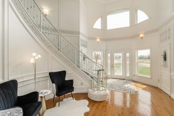 A spacious interior with a grand staircase, elegant chairs, and a large glass enclosure.