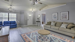 Ein Wohnzimmer mit blauem Sofa, beigem Sofa, Couchtisch und einem gemusterten Teppich. Es gibt Deckenventilatoren, eine Chandelier und gerahmte Kunstwerke an den Wänden.