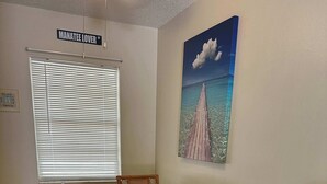 A dining area with a glass-top table, wicker chairs, a small side table, and a painting of a coastal scene. - Professor Rousseau's Manatee Bay (Crystal River)