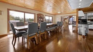 A spacious dining area with wooden flooring and a high ceiling, featuring a central table with chairs and a staircase leading to an upper level. - Crestview Estate 5 acres-heated pool-5min to strip (Pigeon Forge)
