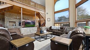 A spacious living area with a stone fireplace, leather sofas, and a large TV. - Crestview Estate 5 acres-heated pool-5min to strip (Pigeon Forge)