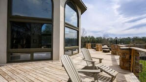 A wooden deck with Adirondack chairs, a stone fireplace, and large windows overlooking a landscape. - Crestview Estate 5 acres-heated pool-5min to strip (Pigeon Forge)