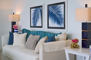 Een woonkamer met een witte bank, kussens in teal-kleur en kunstwerken in lijsten aan de muur.