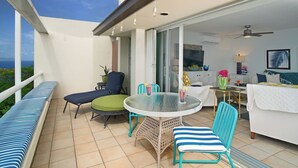 A balcony with a sofa, chairs, a table, and a TV in the background. - Ocean Views | Near Magen’s Bay w/ Pool & Generator (Northside)