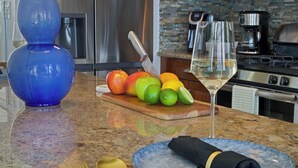 A kitchen counter with fruits, a wine glass, and a blue plate with a napkin.