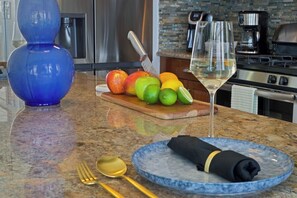A kitchen counter with fruits, a wine glass, and a blue plate with a napkin. - Ocean Views | Near Magen’s Bay w/ Pool & Generator (Northside)