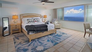 A bedroom with a bed, bedside lamps, a chair, a large window, and a ceiling fan. - Ocean Views | Near Magen’s Bay w/ Pool & Generator (Northside)