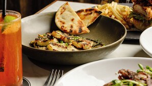 Une table à manger où l’on trouve une variété de plats, notamment des légumes grillés, un hamburger et une assiette de viande accompagnée de légumes.