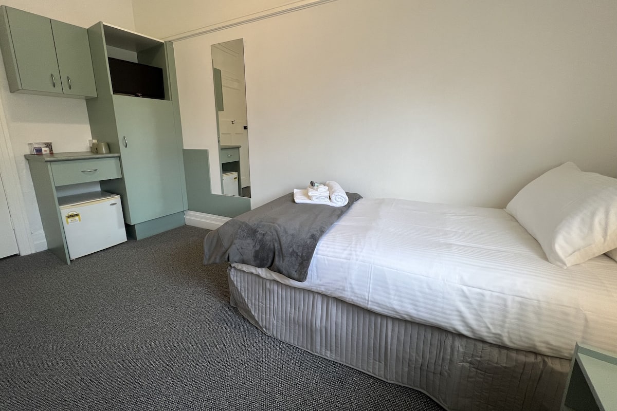 A hotel room with a bed, a desk with a mirror, and a small storage unit.