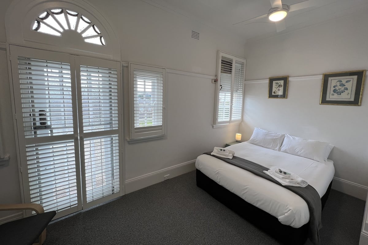 A hotel room with a bed, a nightstand, a lamp, and a window with blinds.
