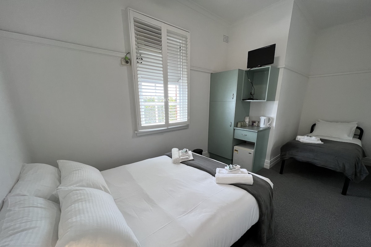 A hotel room with a bed, a desk, a chair, a small cabinet, and a television.