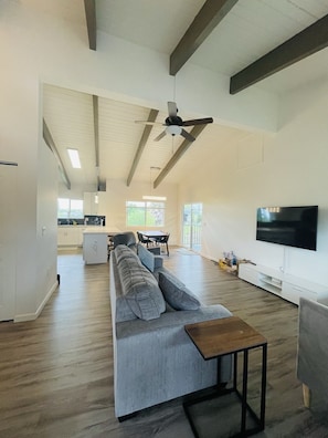 Un salón espacioso con un sofá seccional gris grande, una mesa de centro de madera y un televisor de pantalla plana montado en la pared.