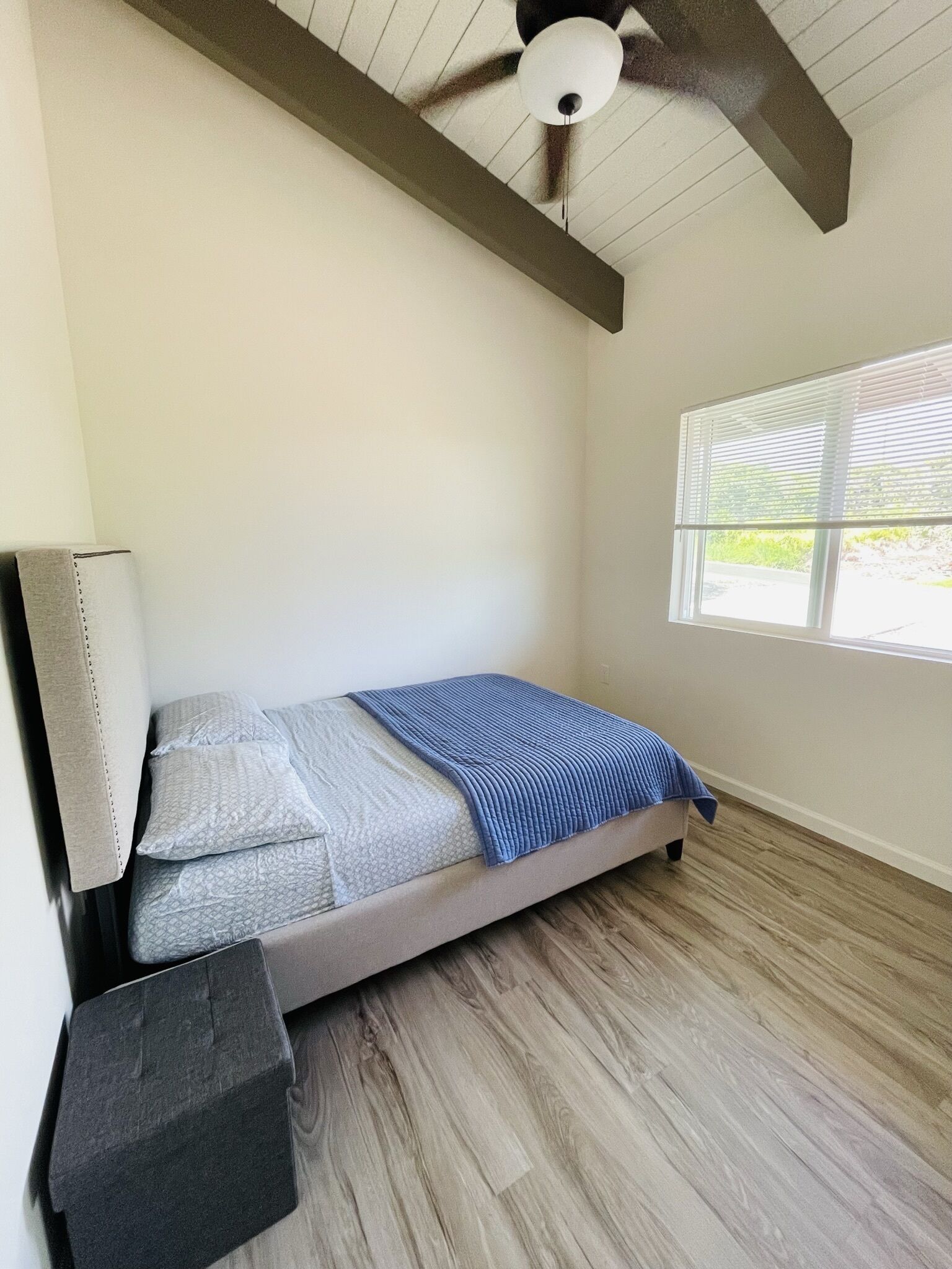 Ein kleines Zimmer mit einem Einzelbett, geneigten Decken, einem Fenster mit Jalousien und Holzboden.