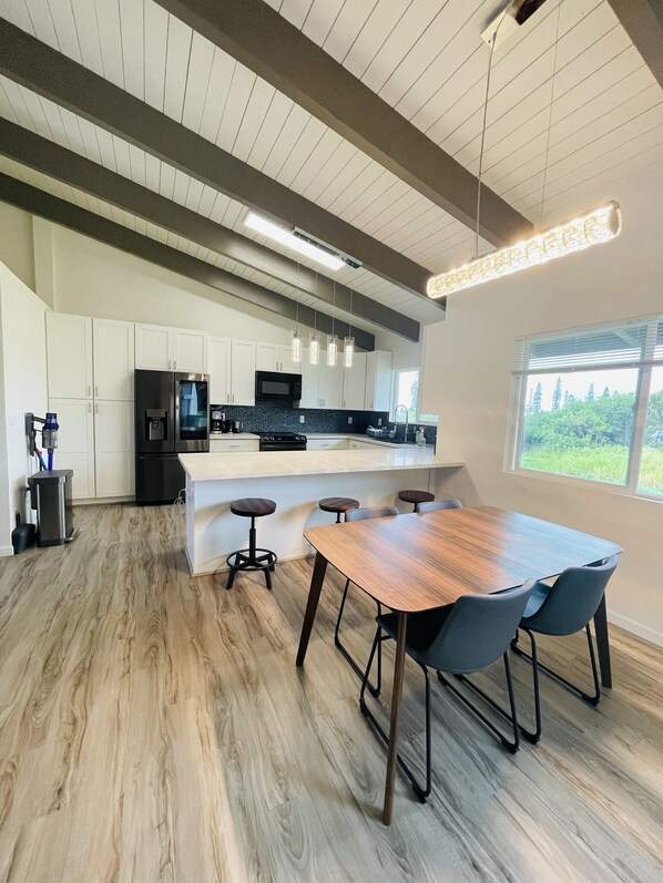 A modern kitchen with white cabinets, a stainless steel refrigerator, a microwave, and a large island with bar stools.
