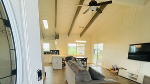 A spacious living area with a grey sofa, a wooden coffee table, and a TV mounted on the wall. - Big Island Green Sands House (Naalehu)