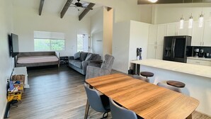 A modern kitchen with white cabinets, a black refrigerator, and a wooden dining table with chairs. - Big Island Green Sands House (Naalehu)