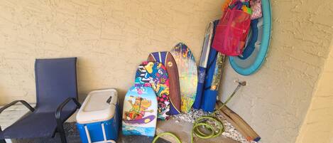 A corner with a blue chair, a blue cooler, colorful bags, a blue inflatable ring, and a green hose.
