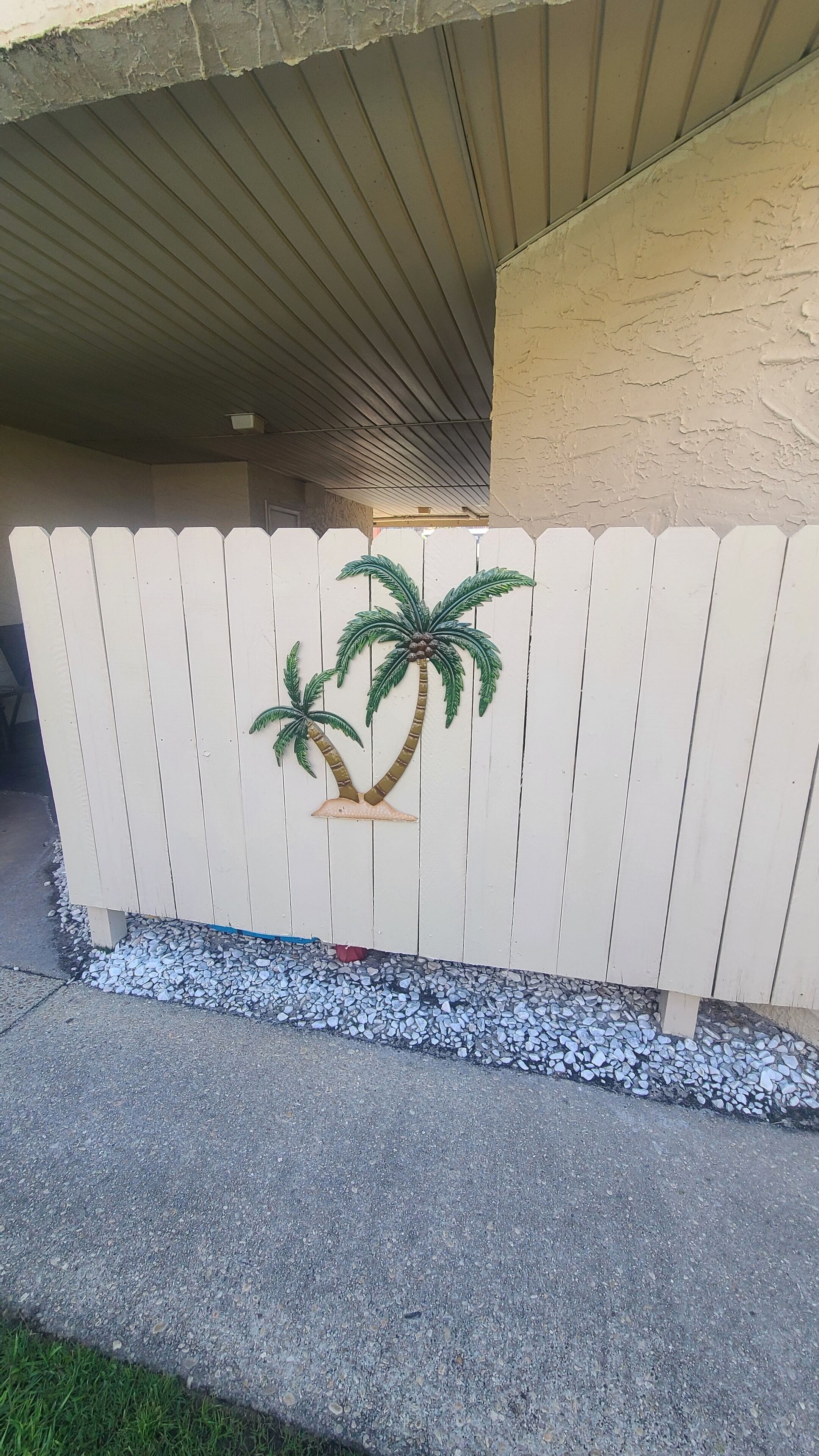 A white picket fence with palm trees and a concrete pathway.