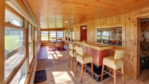 A wooden interior with a bar area, bar stools, and large windows. - 600' of Green Bay Frontage & Dock: Cozy Cottage (Oconto)
