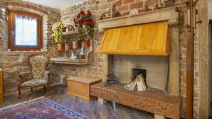 Una habitación de paredes de piedra con chimenea, una silla de madera y una alfombra.