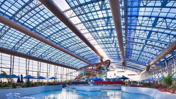 An indoor water park with a glass ceiling, slides, and a pool area.