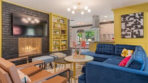 A modern living room with a blue sofa, a yellow bookshelf, and a flat-screen TV mounted on a brick wall.
