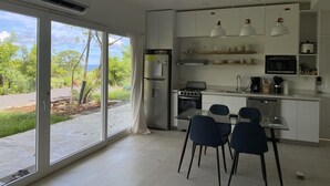 A modern kitchen with a dining area, large windows, and a view of greenery. - Ocean View 1 BR w/Office, Rooftop and Gardens (Playas del Coco)