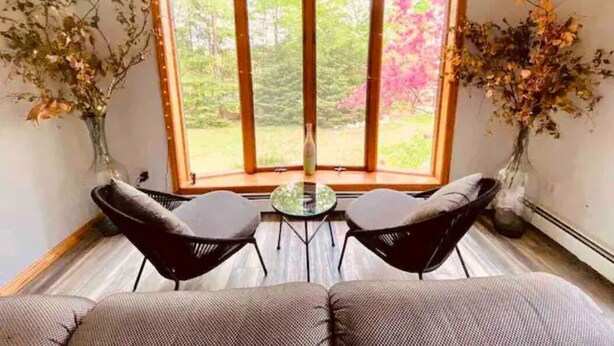 A room with a large window, two black chairs, a small table, and a sofa. - Spacious Riverfront Getaway in the Heart of the White Mountains (Carroll)