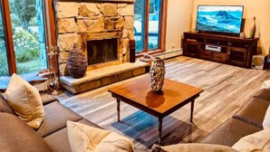 A living room with a stone fireplace, a television, and a sofa. - Spacious Riverfront Getaway in the Heart of the White Mountains (Carroll)