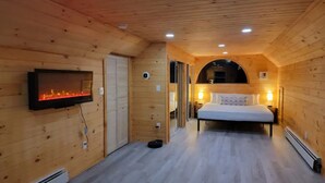 A wooden cabin with a bed, a TV, and a fireplace. - Spacious Riverfront Getaway in the Heart of the White Mountains (Carroll)