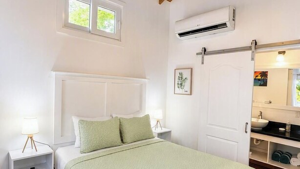 Un dormitorio con techo de madera, una cama con cubrecama verde, una mesita de noche con lámpara y un equipo de aire acondicionado.