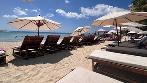 Una playa con sillas de madera y sombrillas, arena y el océano al fondo.