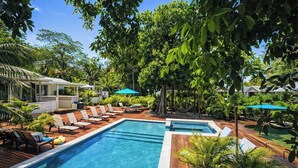 A pool area with lounge chairs and umbrellas, surrounded by lush greenery. - Adorable studio style casita with all the comforts (West Bay, Roatán)