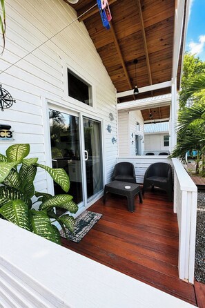 A covered porch with two wicker chairs and a small table, white siding, and a wooden ceiling.