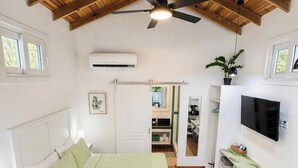 A bedroom with a bed, a ceiling fan, an air conditioning unit, a television, and a plant. - Adorable studio style casita with all the comforts (West Bay, Roatán)