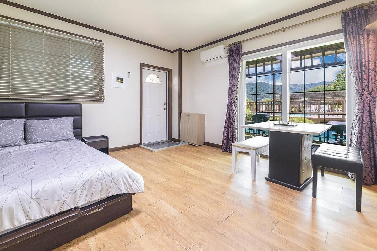 A bedroom with a bed, a desk, and a view of a mountainous landscape through large windows.