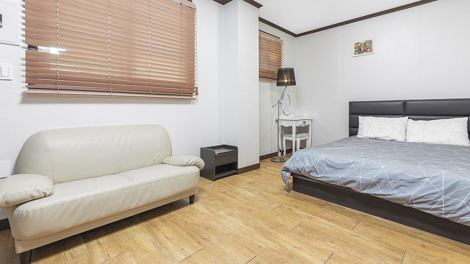 A bedroom with a bed, a sofa, a bedside table, a lamp, and a mirror.