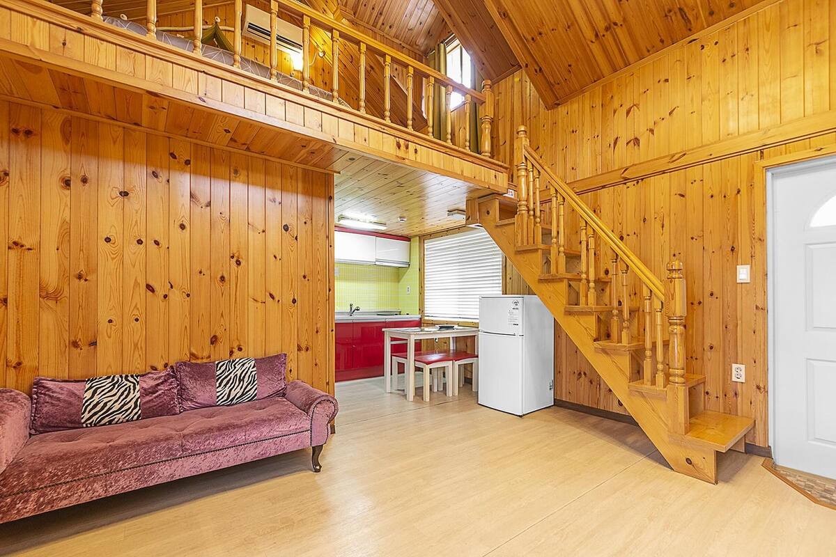 A wooden interior with a sofa, a dining table, and a kitchen area.